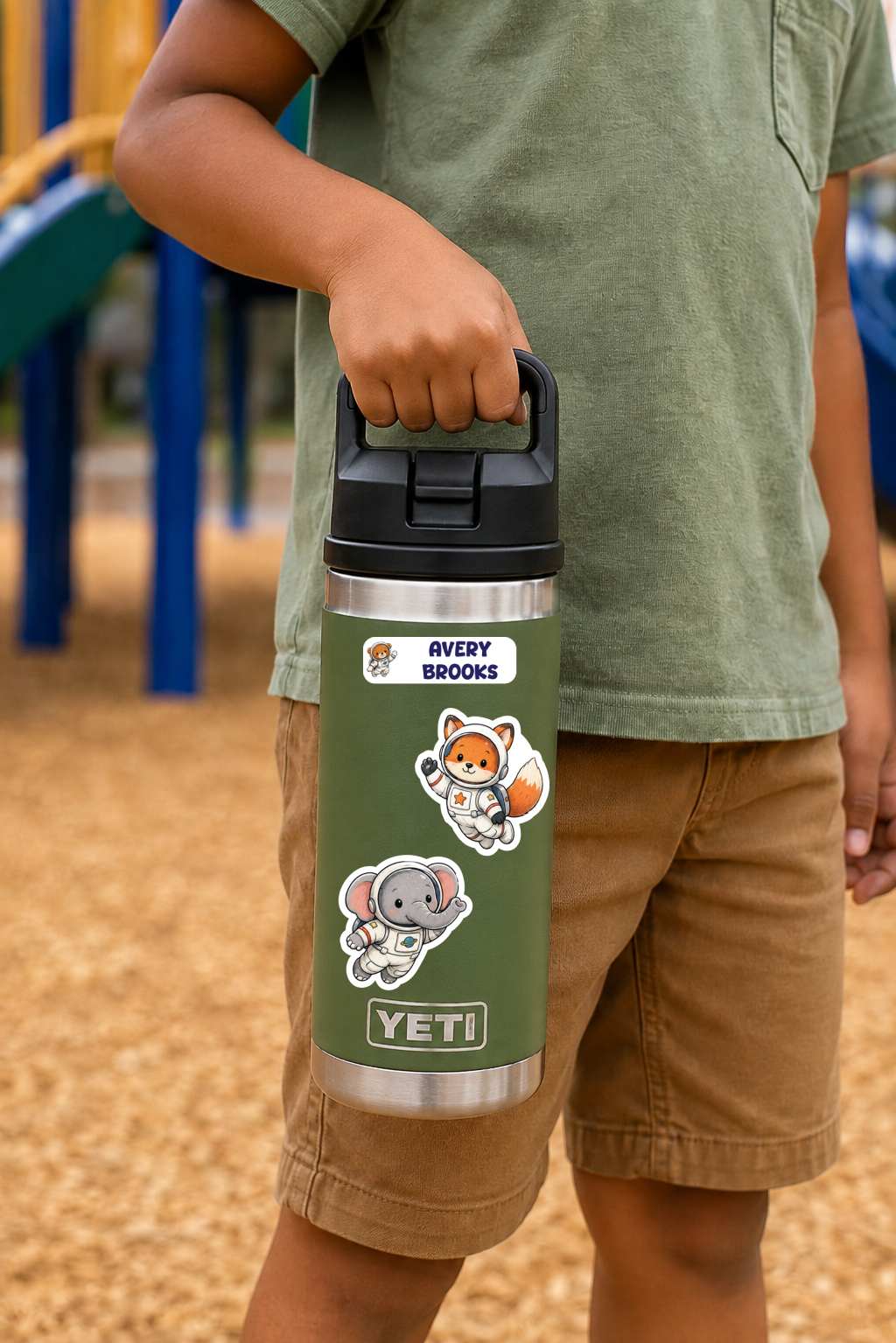 A child outdoors at a playground holding a green Yeti water bottle with cartoon animal stickers, including a fox and an elephant, and a 'Every Brooks' label.