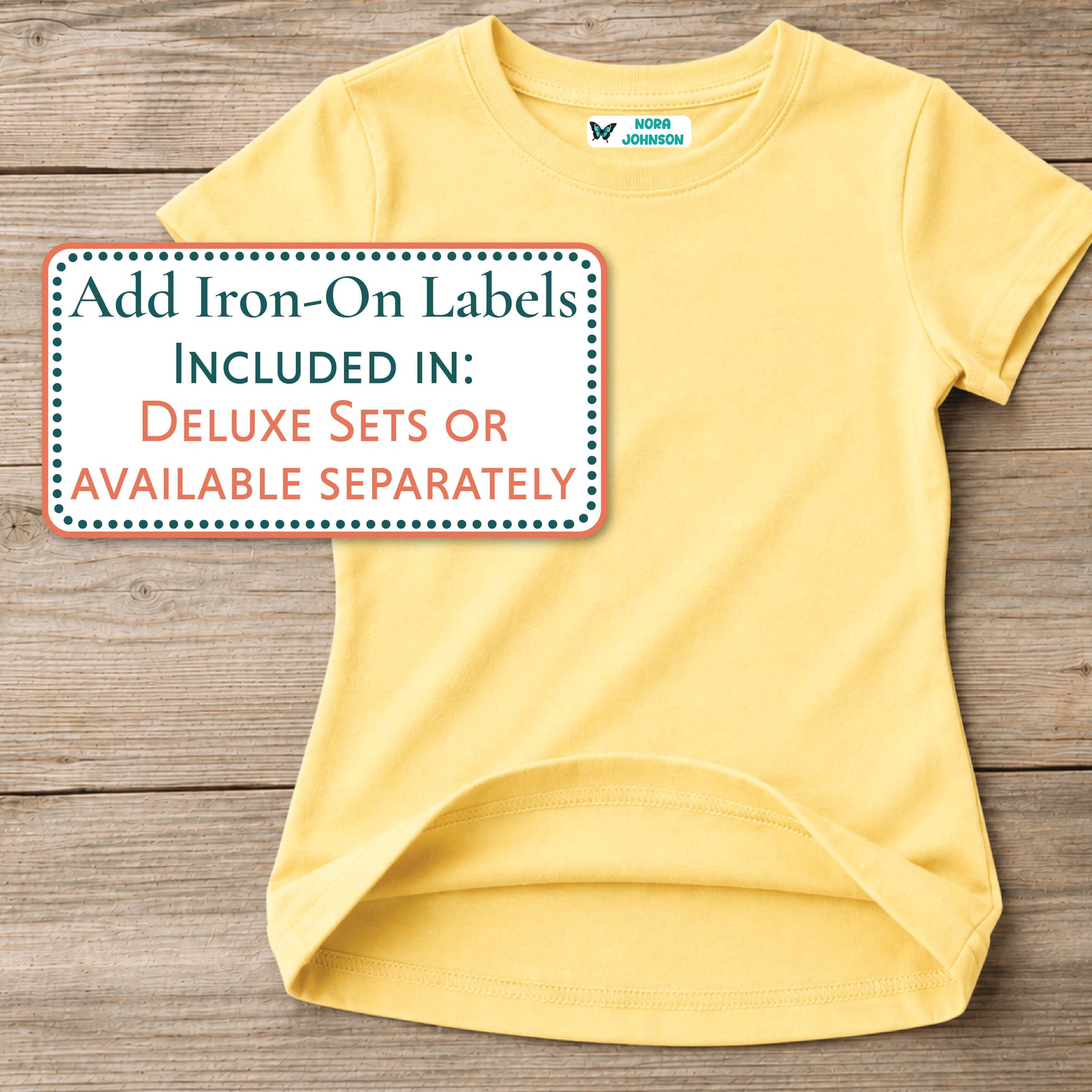 A light yellow short-sleeve t-shirt laid flat on a rustic wooden background, with a white text box overlaid on the left that reads, 'Add Iron-On Labels INCLUDED IN: Deluxe Sets or Available Separately.' A small neck label reading Nora Johnson is visible inside the collar.