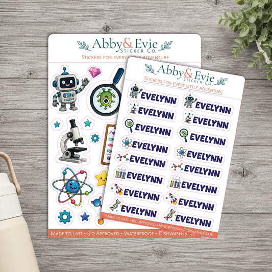 Two sheets of Abby & Evie sticker set stickers for 'Every Little Adventure' displayed on a gray wood background with a plant and part of a mug visible.