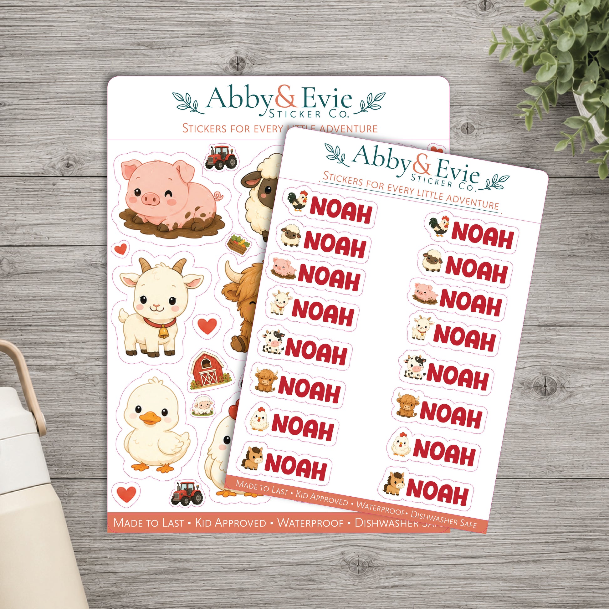 Two sheets of Abby & Evie sticker characters on a gray wooden tabletop, with a small plant and part of a cream bag visible around the edges. The front sheet shows repeated 'NOAH' text labels with small animal illustrations, and the back sheet shows larger animal stickers including a pig, goat, cow, duck, tractor, barn, and red hearts.
