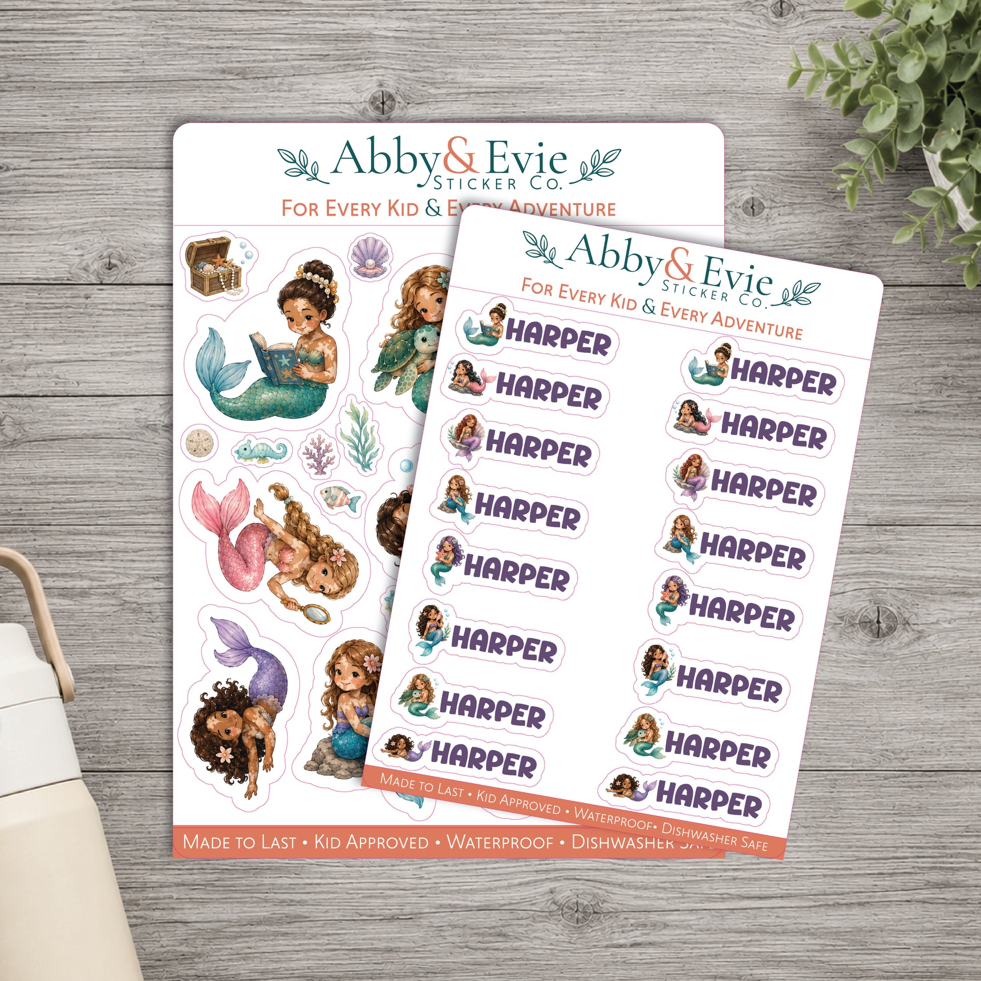 Two sticker sheets from Abby & Evie Sticker Co. featuring mermaid-themed designs and the name 'Harper' repeated, arranged on a gray wood surface with a small plant and part of a bag visible at the edges.