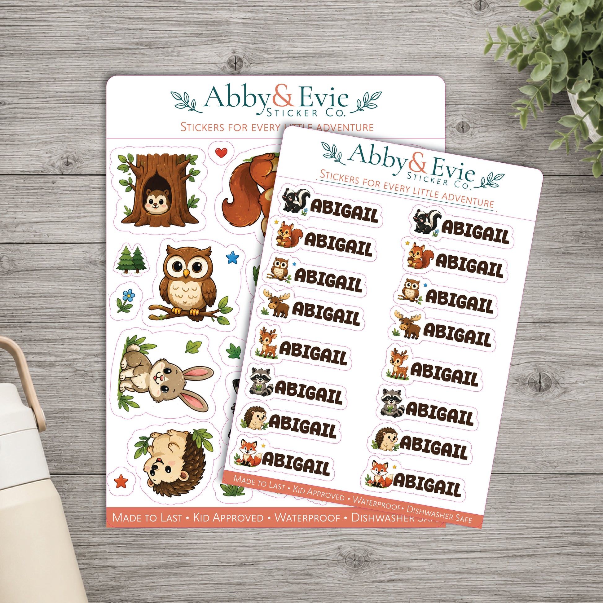 Two sticker sheets from Abby & Evie Sticker Co. displayed on a gray wood surface, with one sheet featuring cartoon animal illustrations and the other featuring repeated 'ABIGAIL' name stickers.