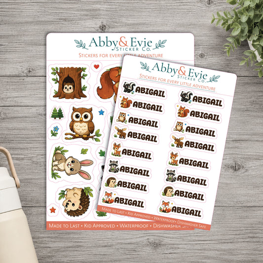 Two sticker sheets from Abby & Evie Sticker Co. displayed on a gray wood surface, with one sheet featuring cartoon animal illustrations and the other featuring repeated 'ABIGAIL' name stickers.