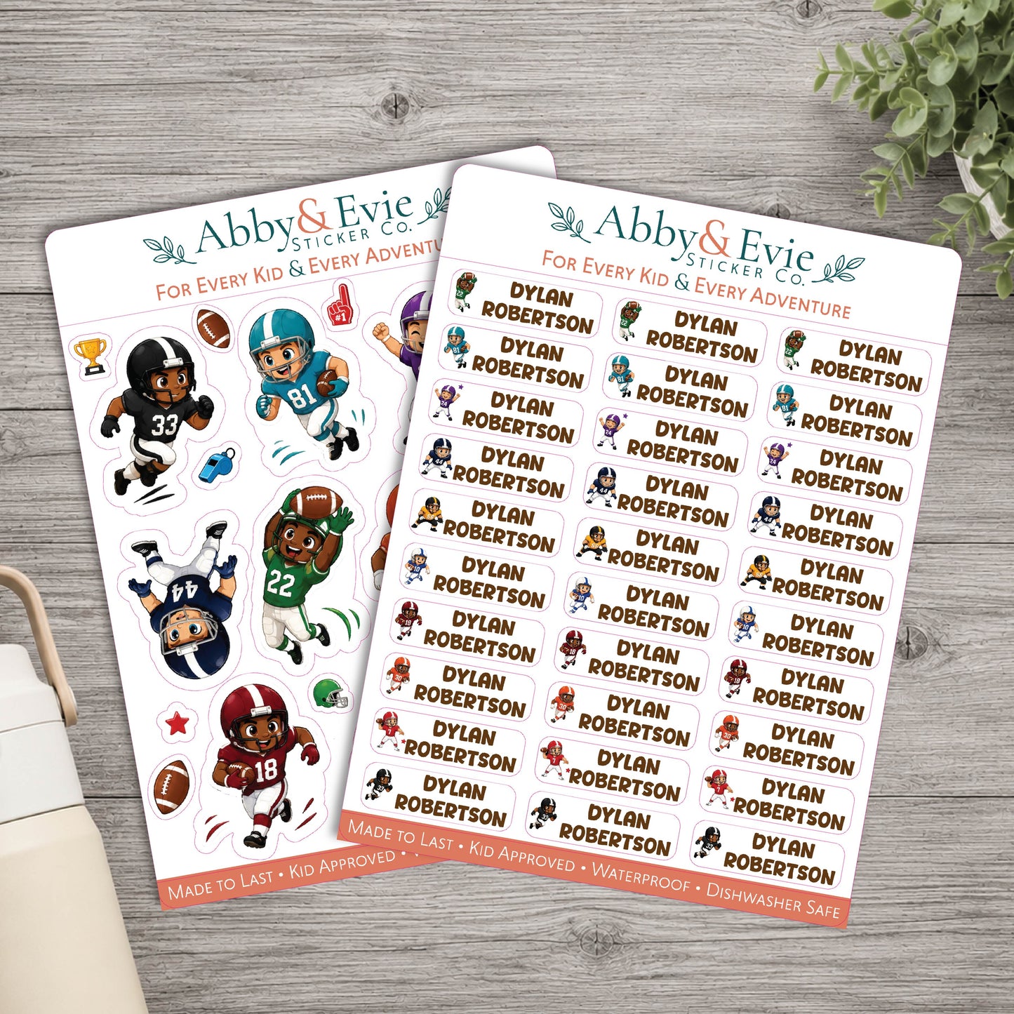 Two sticker sheets from Abby & Evie Sticker Co. featuring cartoon football player characters named Dylan Robertson in various uniforms and poses, displayed on a gray wood background with a book corner and greenery visible.
