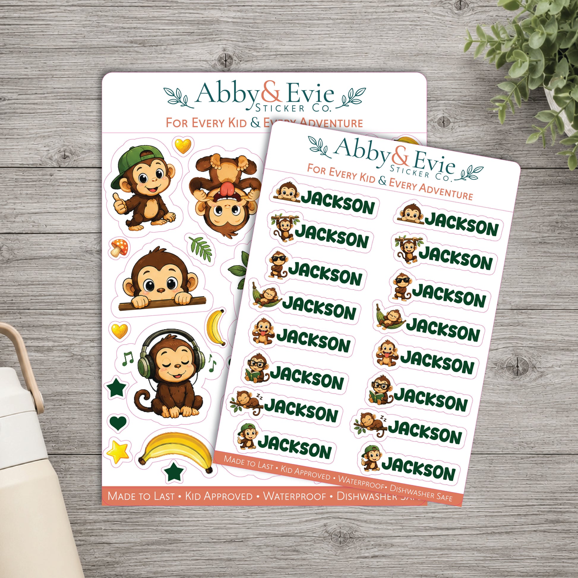 Two sticker sheets from Abby & Evie Sticker Co. featuring cartoon monkey illustrations and the name 'Jackson' repeated, displayed on a gray wood surface with a small plant and part of a bag visible.