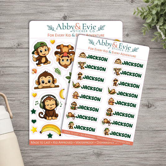 Two sticker sheets from Abby & Evie Sticker Co. featuring cartoon monkey illustrations and the name 'Jackson' repeated, displayed on a gray wood surface with a small plant and part of a bag visible.