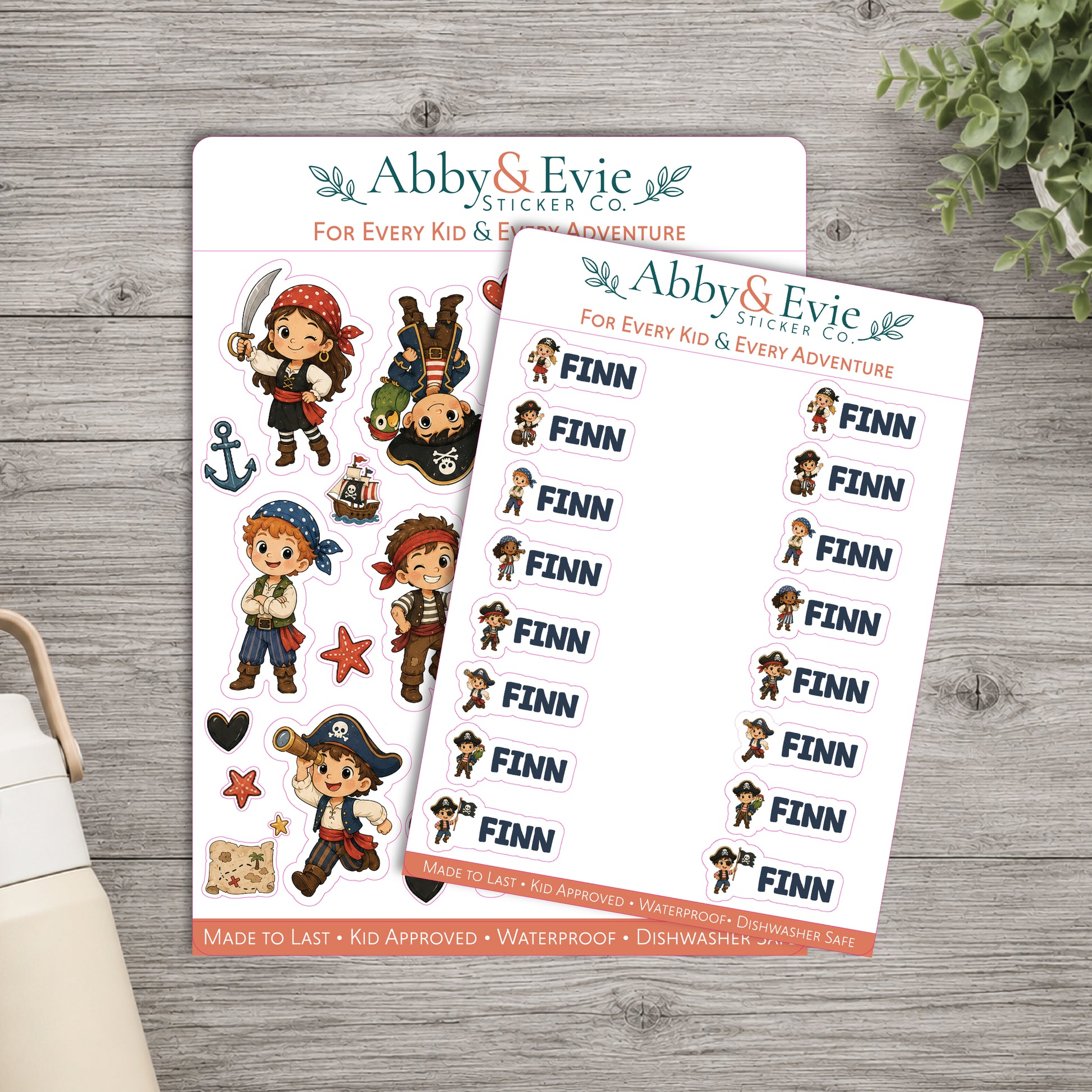 Two printable sticker sheets from Abby & Evie Sticker Co. featuring pirate-themed cartoon characters and repeated 'FINN' labels, arranged on a gray wood surface with a small plant and part of a bag visible at the edges.