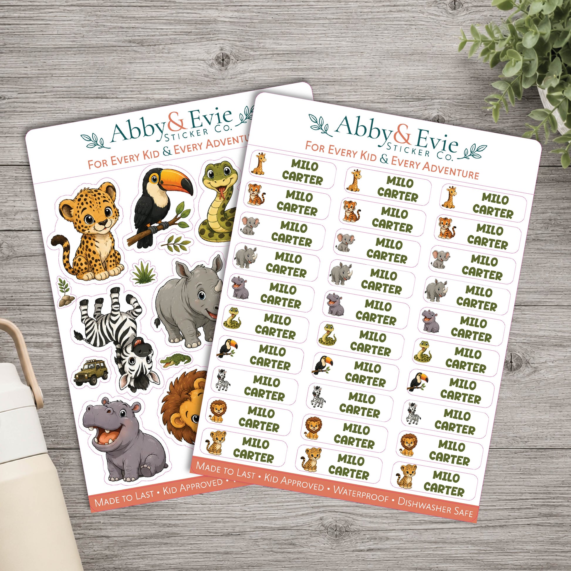 Two sheets of Abby & Evie Sticker Co. safari-themed stickers on a gray wooden tabletop, with a small vase and greenery in the background.
