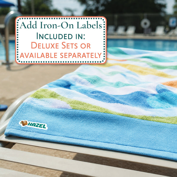 A multicolor beach towel with a blue border and a small LIAM logo is draped over a poolside lounge chair, with a text overlay explaining iron-on label options.