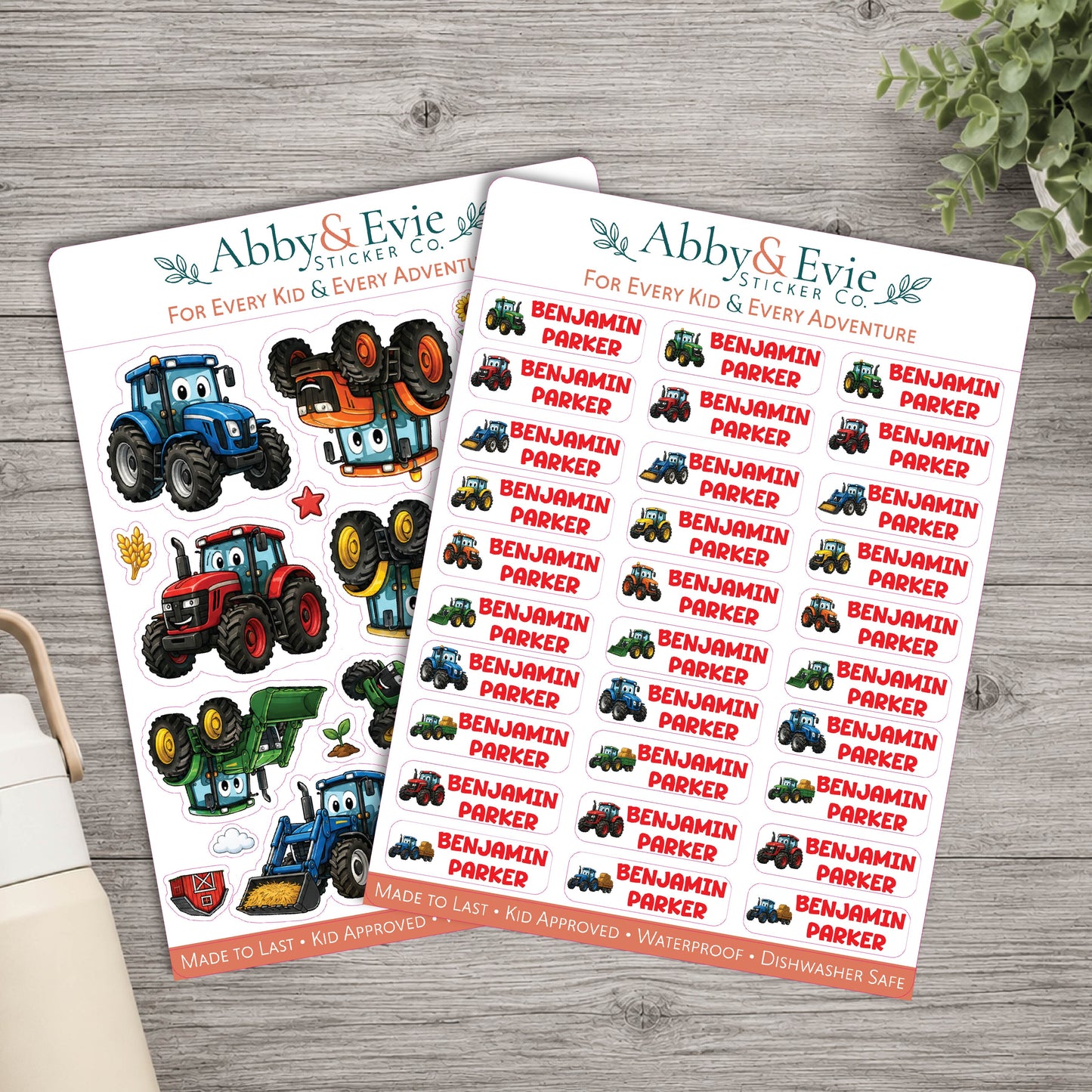 Two sheets of Abby & Evie Sticker Co. tractor-themed stickers displayed on a gray wooden tabletop, with a small plant leaf in the top right corner.