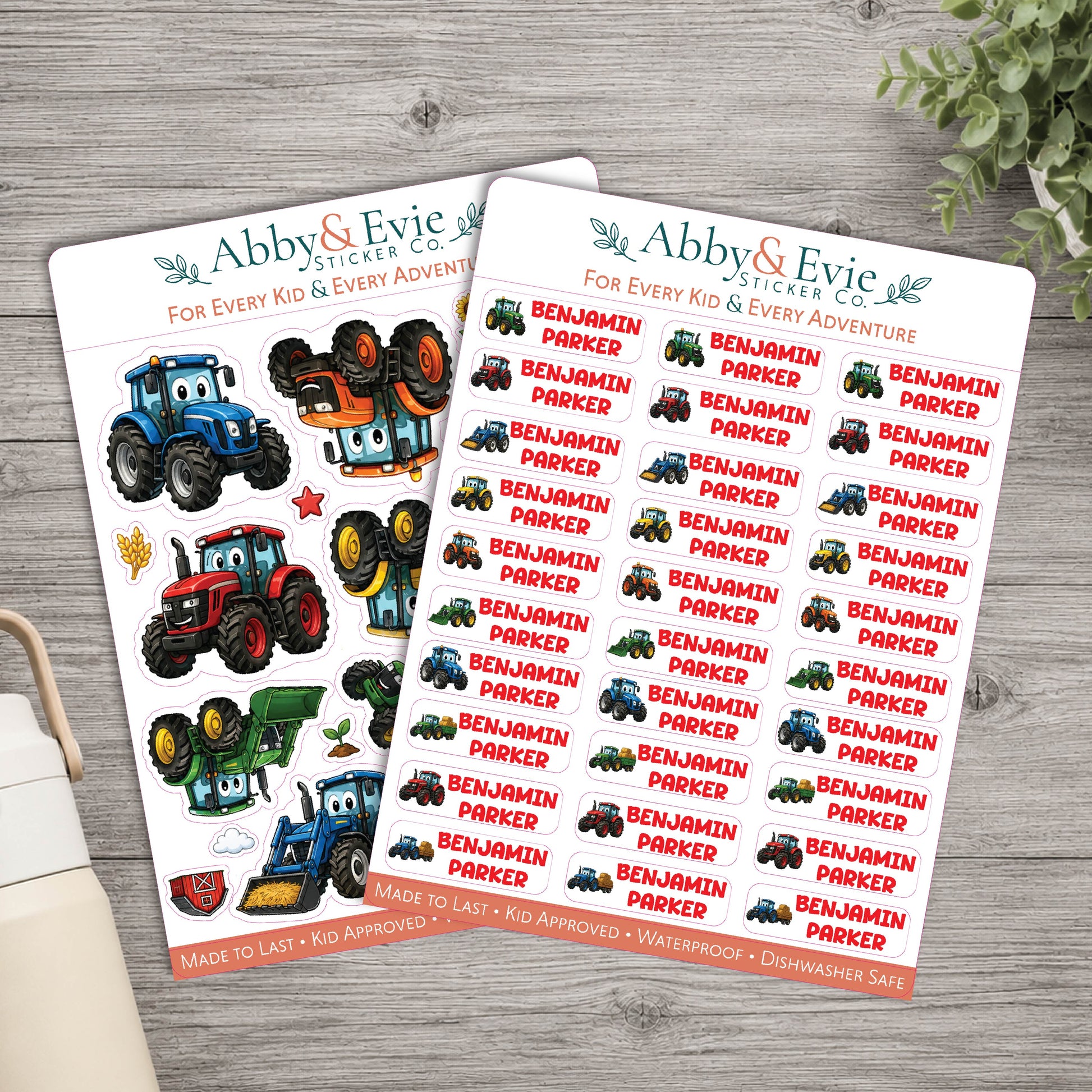 Two sheets of Abby & Evie Sticker Co. tractor-themed stickers displayed on a gray wooden tabletop, with a small plant leaf in the top right corner.