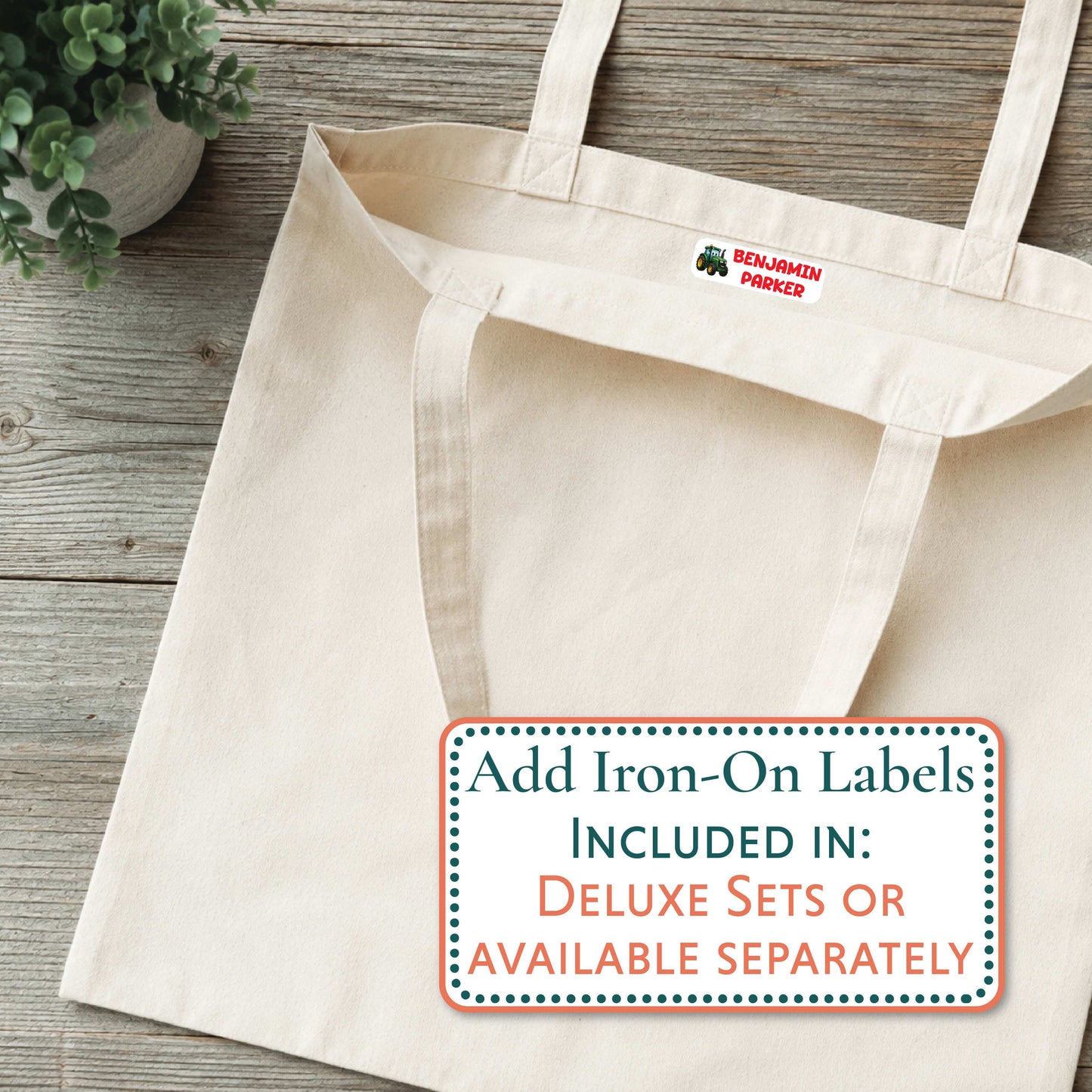 A natural canvas tote bag laid flat on a rustic wood surface, with a small red and green 'BENJAMIN PARKER' logo printed inside the collar. A white promotional label at the bottom reads, 'Add Iron-On Labels INCLUDED IN: DELUXE SETS OR AVAILABLE SEPARATELY.