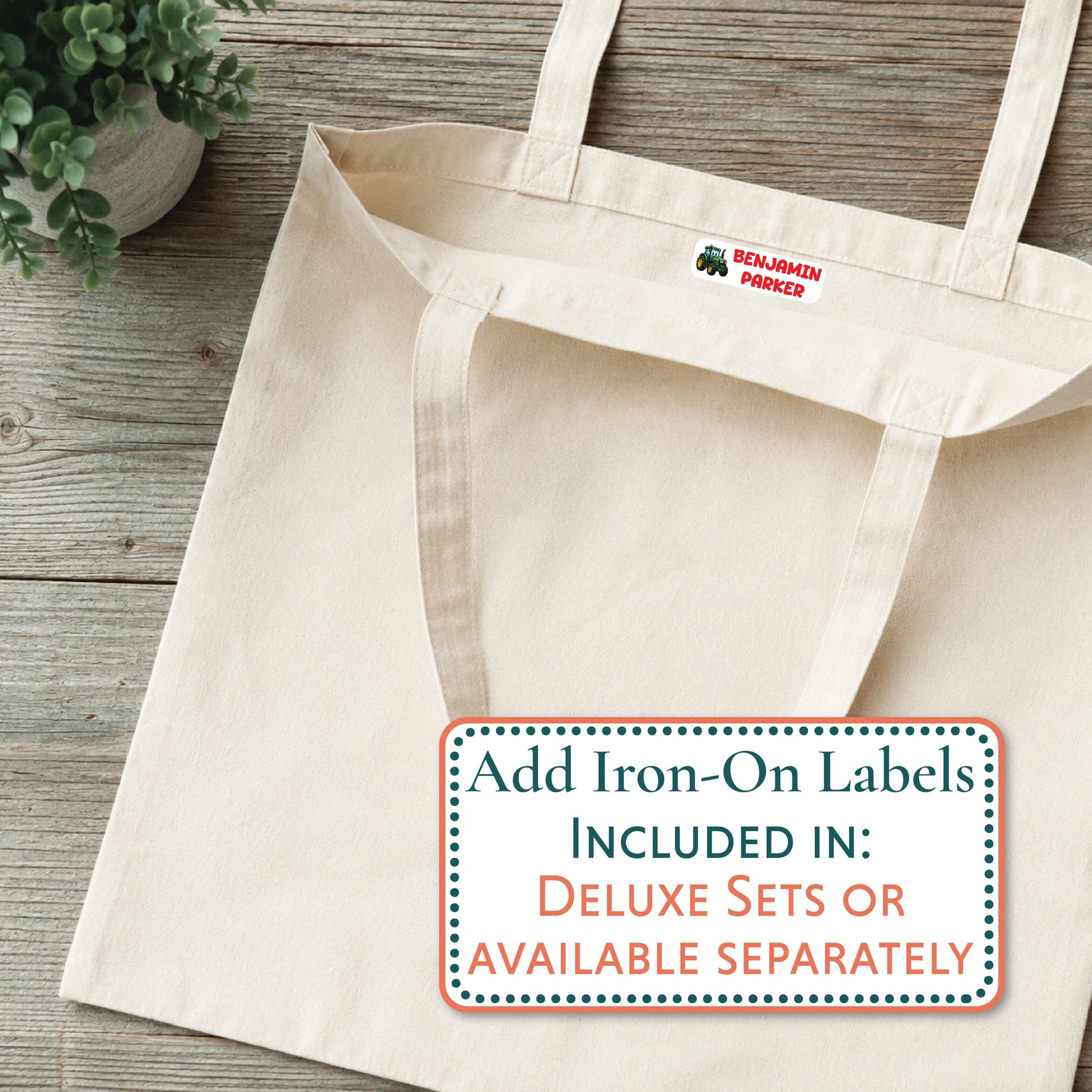 A natural canvas tote bag laid flat on a rustic wood surface, with a small red and green 'BENJAMIN PARKER' logo printed inside the collar. A white promotional label at the bottom reads, 'Add Iron-On Labels INCLUDED IN: DELUXE SETS OR AVAILABLE SEPARATELY.
