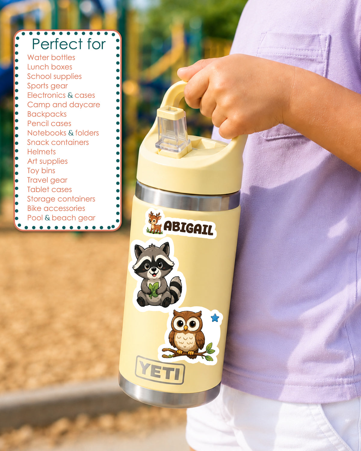 A person in a light purple shirt holds a beige YETI insulated tumbler with a lid. The tumbler has animal decals including a raccoon, owl, and a small fox, plus a sticker reading ABIGAIL.