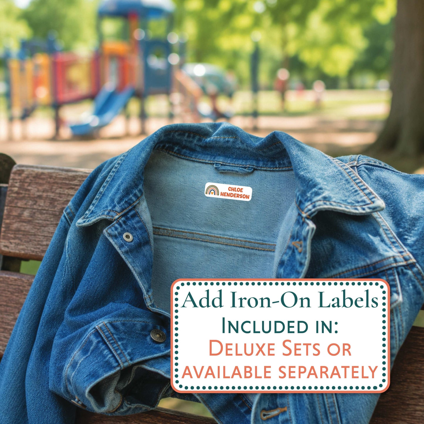 A blue denim jacket draped on a wooden bench in a park, with a visible 'ARTHUR' iron-on label on the collar. A text box in the foreground reads, 'Add Iron-On Labels INCLUDED IN: DELUXE SETS OR AVAILABLE SEPARATELY.