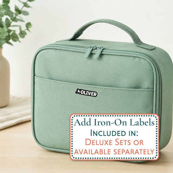 A sage green OLIVER insulated case with a top handle and front zip pocket, shown on a light wood surface with a blurred plant in the background. A promotional text overlay at the bottom right reads, 'Add Iron-On Labels INCLUDED IN: DELUXE SETS OR AVAILABLE SEPARATELY'.