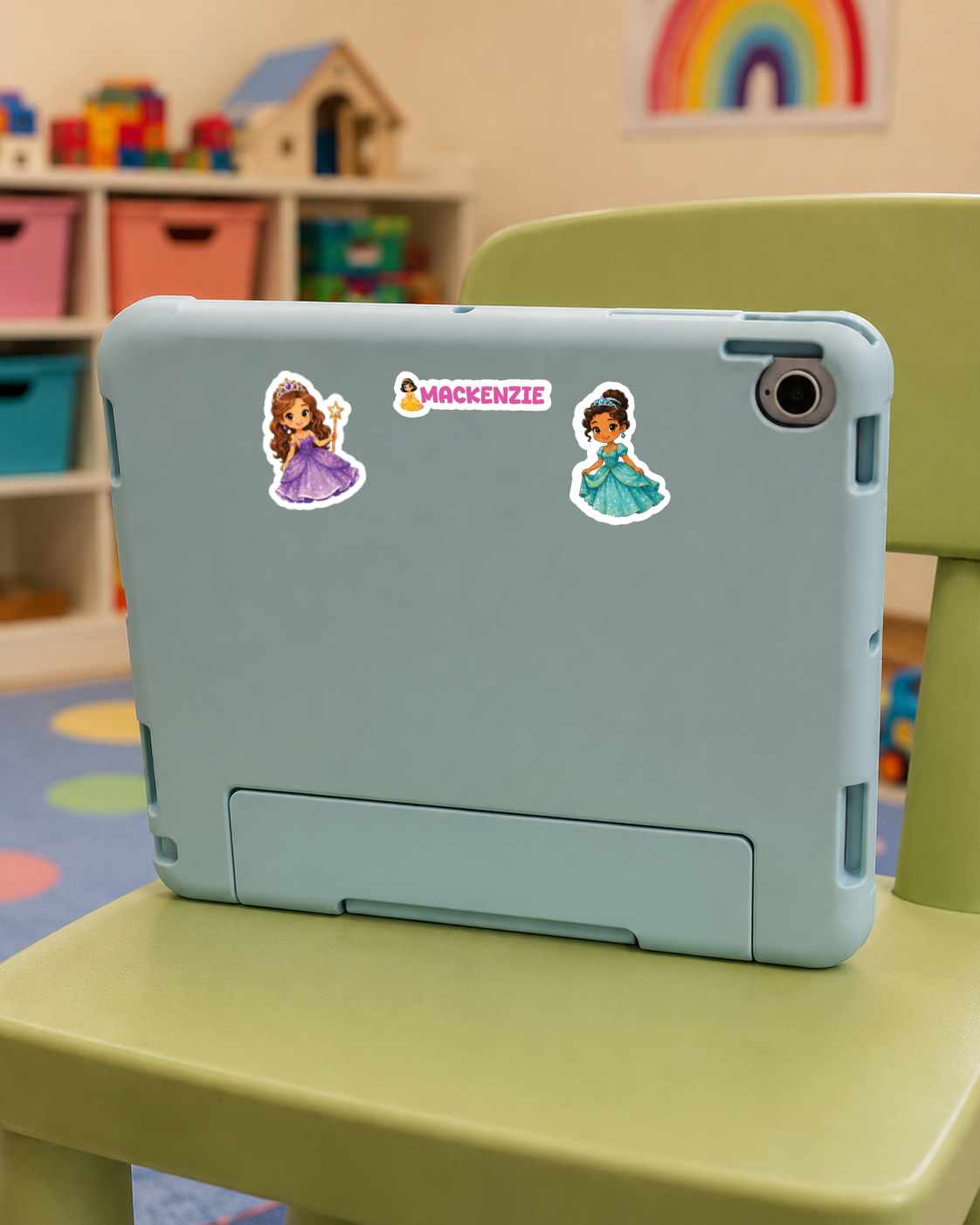 A light blue tablet case with two Disney princess stickers and a 'MACKENZIE' logo decal, shown on a green chair in a child's room.
